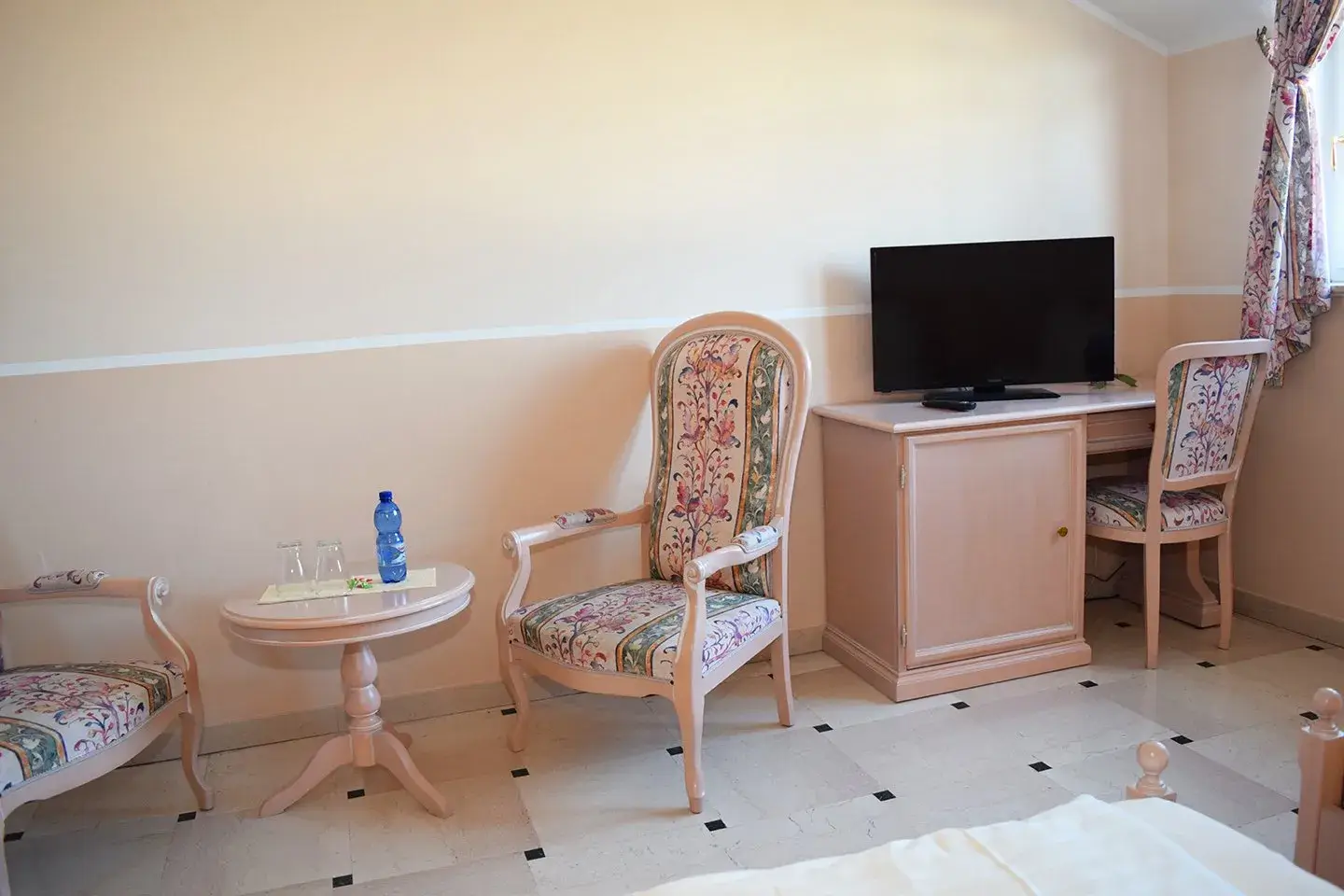 2 Stühle um einen kleinen Tisch neben einem Schreibtisch mit TV Gerät