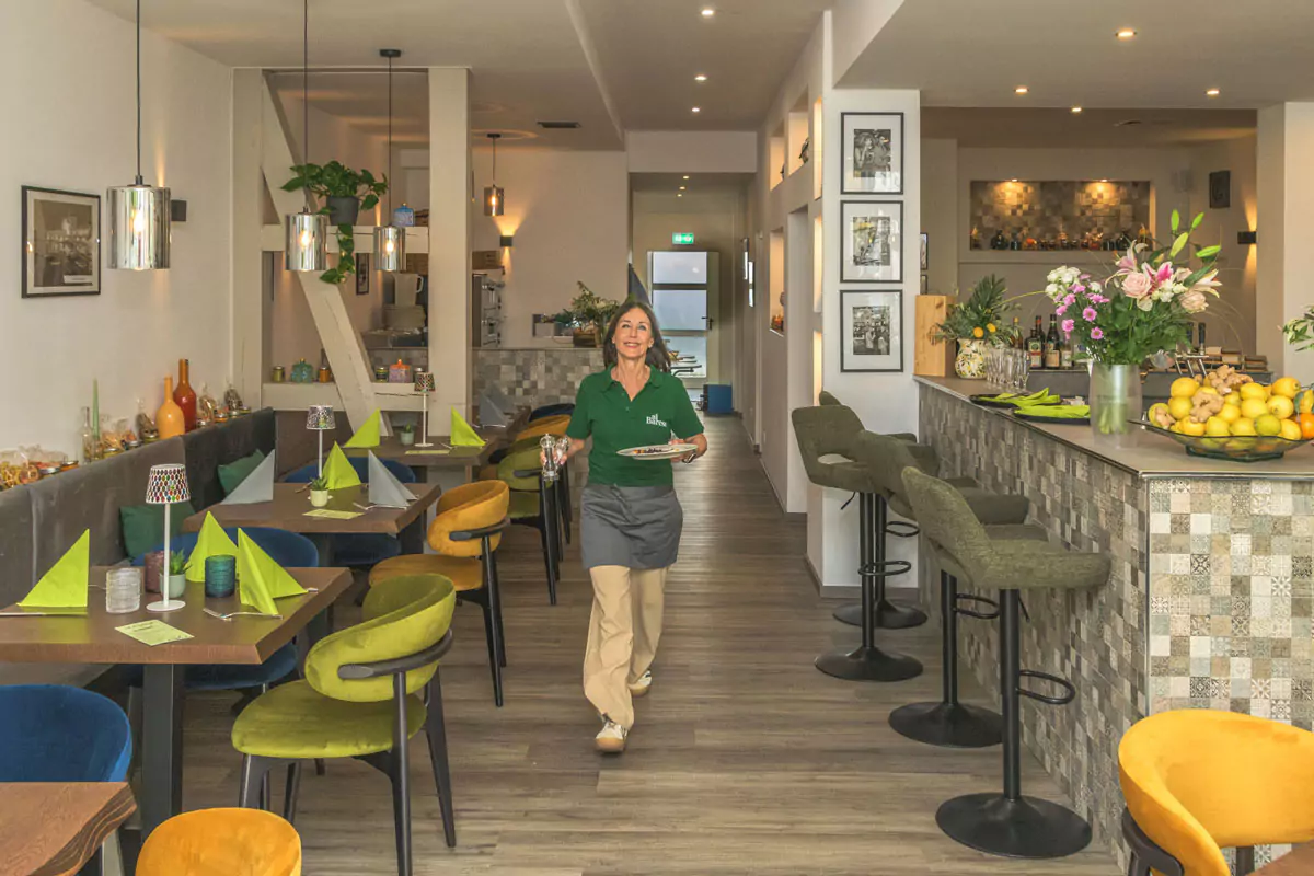 Bedienung mit Teller läuft lächelnd durch den Gästebereich eines Restaurants