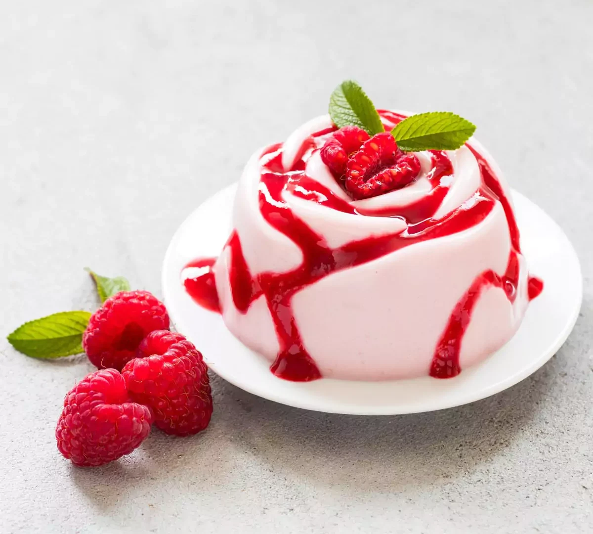 Himbeercreme-Dessert, Panna Cotta in Form einer Rose, mit Himbeersoße, auf einem Teller