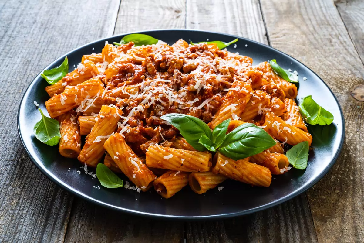 Penne Nudeln mit Hackfleischsauce und Parmesanstreifen mit frischen Basilikumblättern garniert