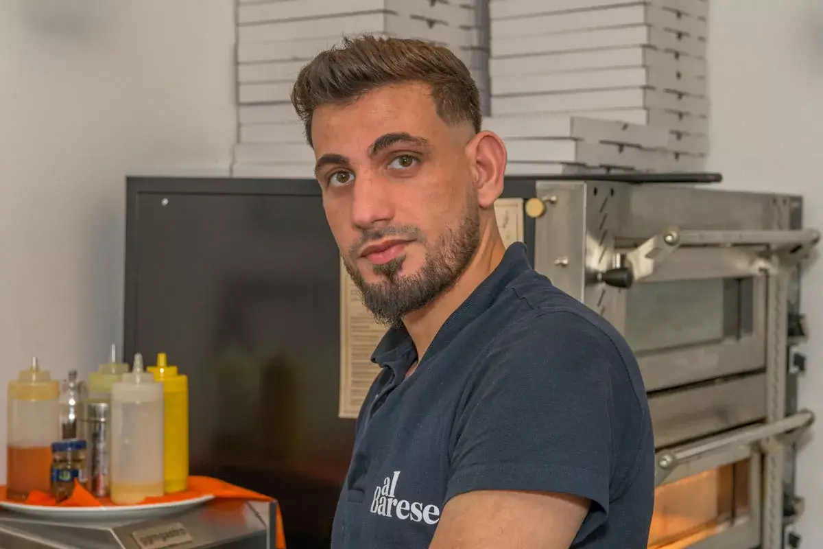 Mann mit dunkelblauem Poloshirt mit Aufschrift 'al barese' steht in einer Küche vor einem Pizzaofen.