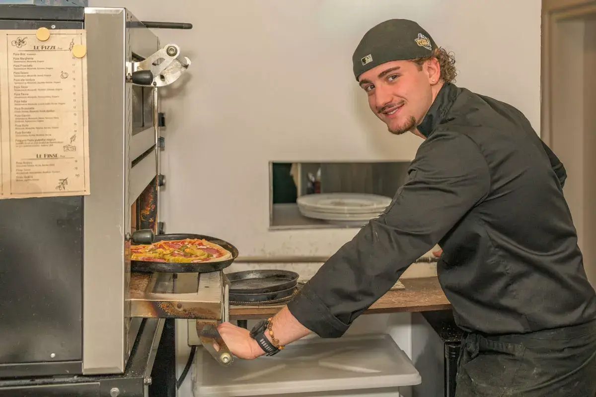 junger Pizzabäcker schiebt eine Pizza in den Pizzaofen