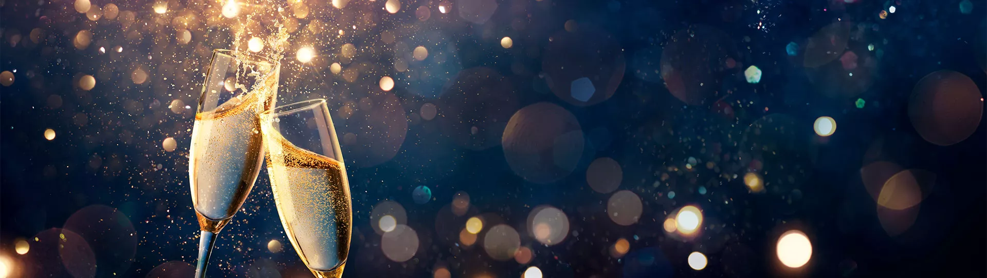 Zwei anstoßende Sektgläser vor unscharfem Hintergrund mit goldenen Lichtpunkten.