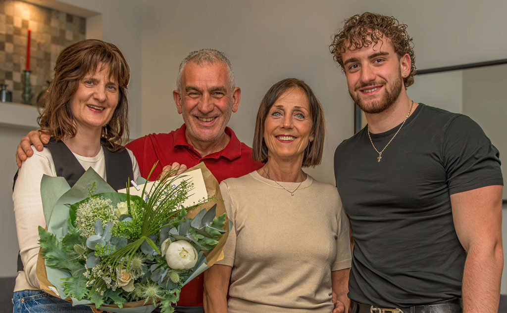 Vier Personen stehen eng beieinander, eine hält einen großen Blumenstrauß mit grünen Blättern und weißen Blüten
